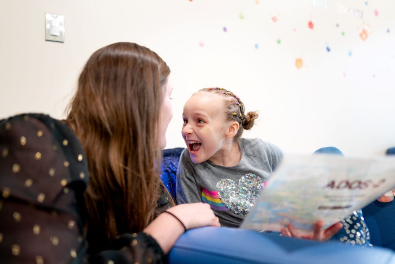 young girl with autism smiling and looking at woman