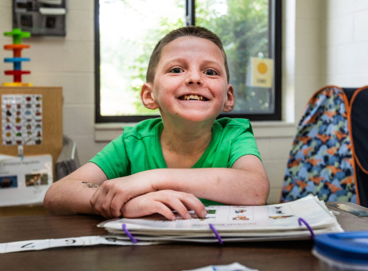 Young boy smiling up at the camera while studying