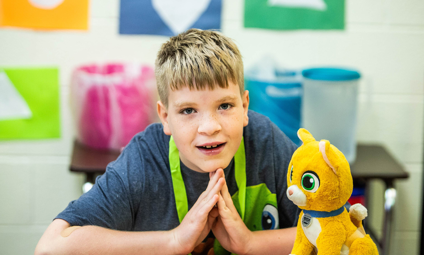 A boy is sitting at the desk, looking at the camera