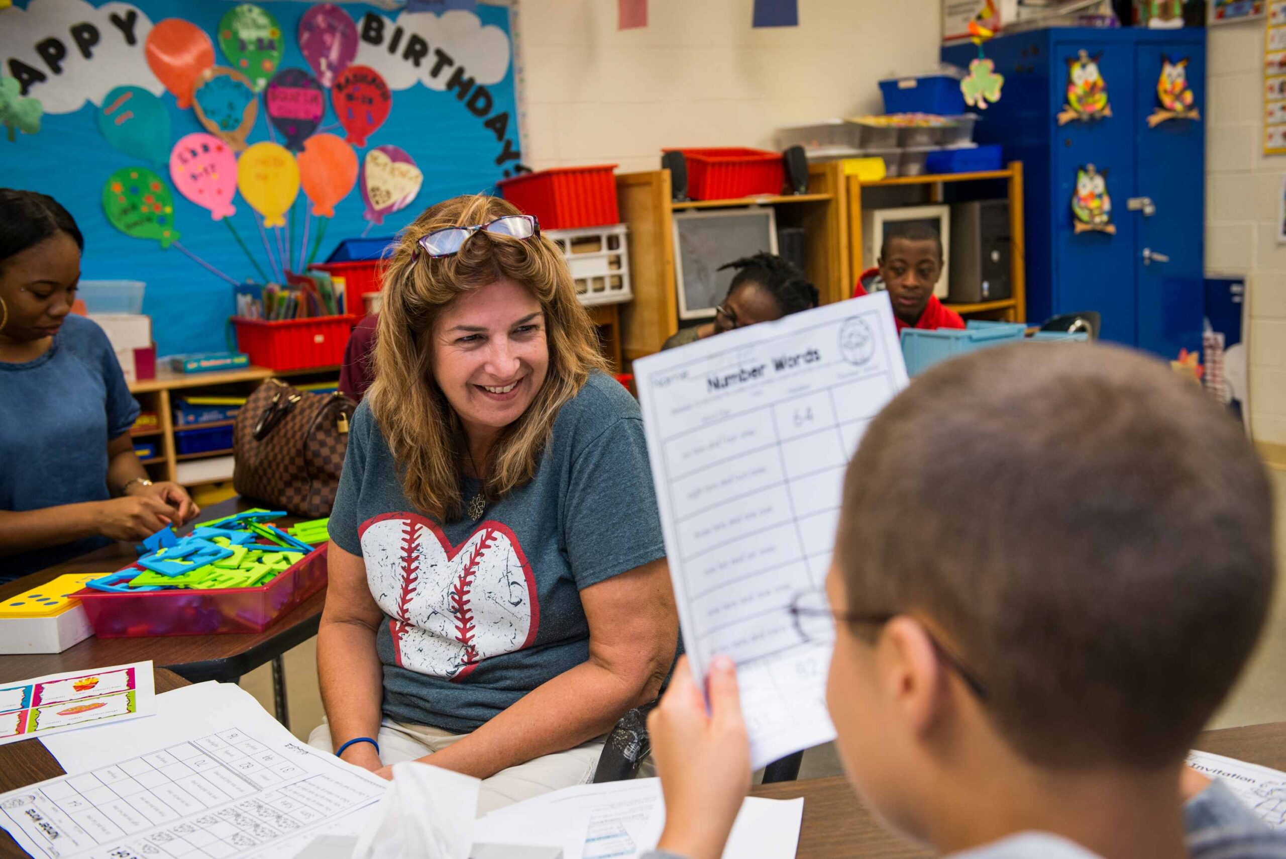 a teacher sitting behind a desk smiling at her student