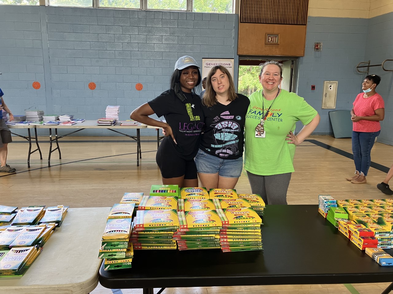 Three women standing at a table covered in school supplies