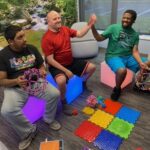 Three men sitting on colorful light-up blocks in a sensory room