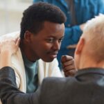 young black man being comforted by a white woman with short blond hair who has her hand on his shoulder