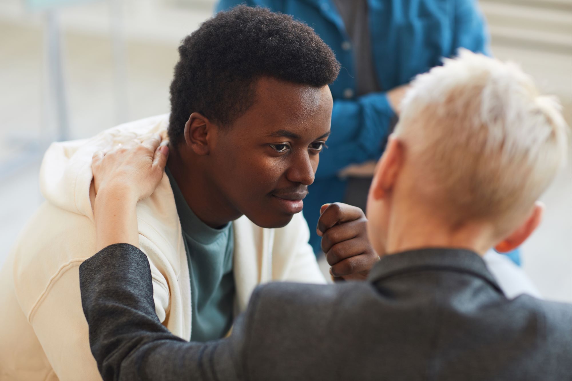 young black man being comforted by a white woman with short blond hair who has her hand on his shoulder