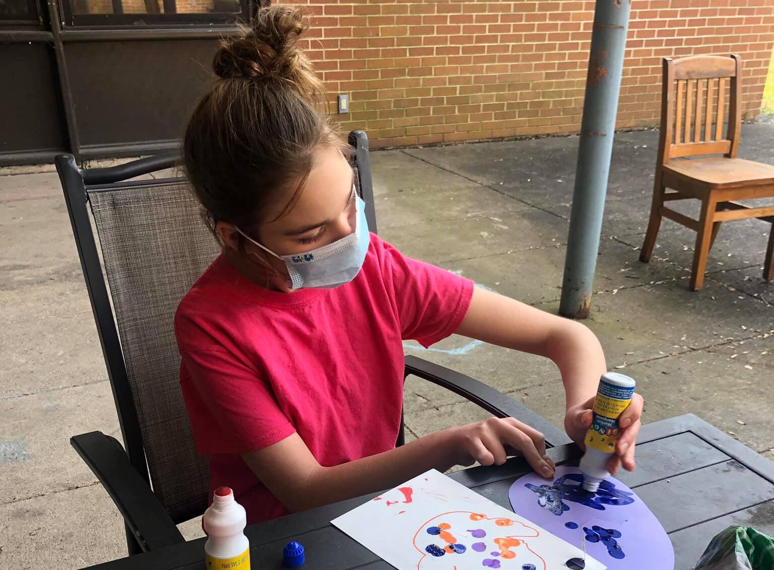 girl wearing a mask sitting at the table making pictures