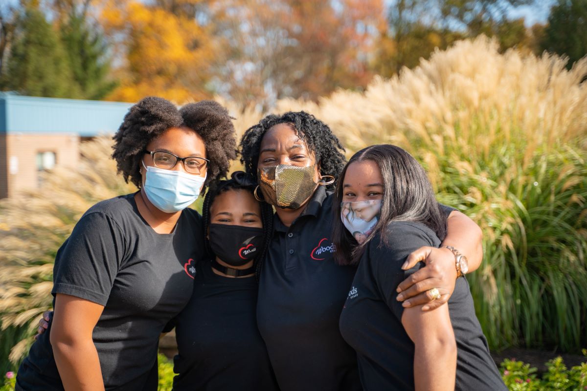 4 women wearing black shirts and masks with their arms around one another