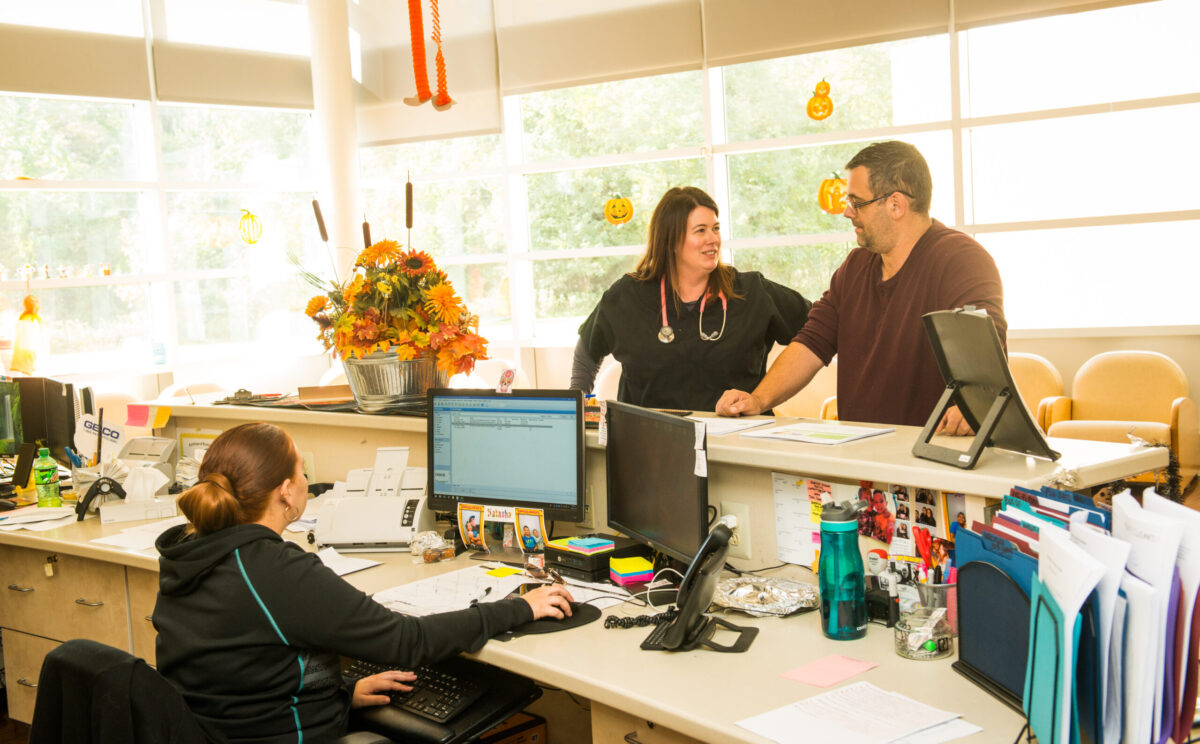 female nurse practitioner leaning on counter speaking to a male employee