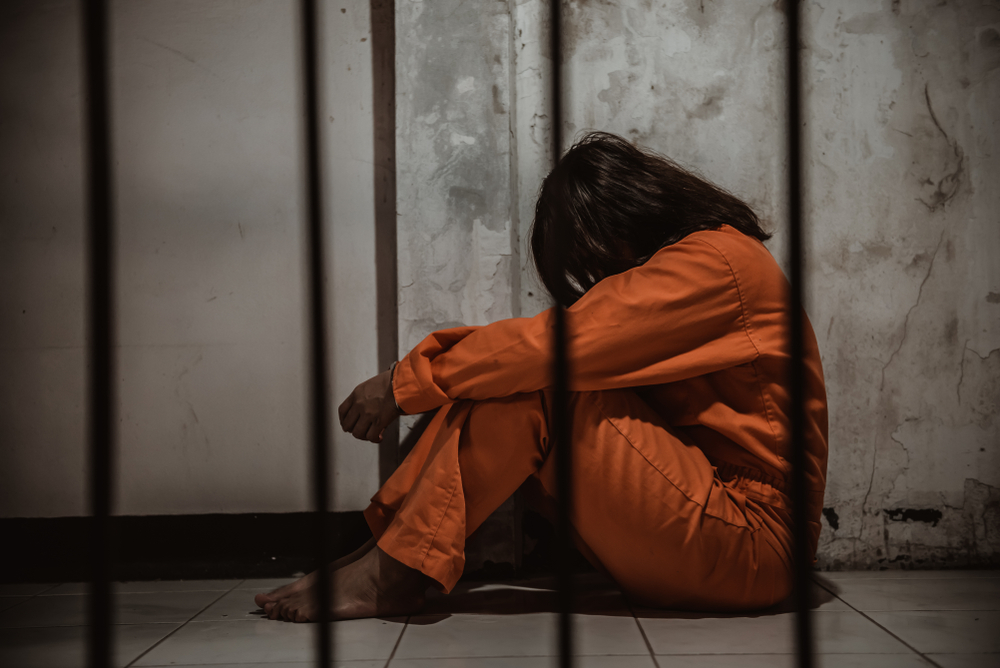 person wearing orange jump suit sitting on floor in prison cell