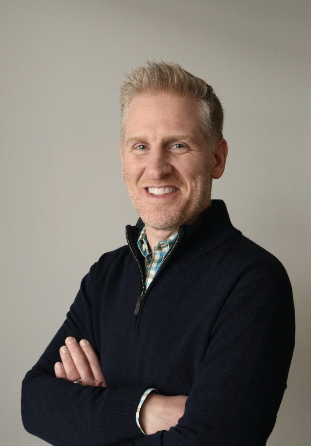 man with short blond hair wearing a dark sweater with his arms folded