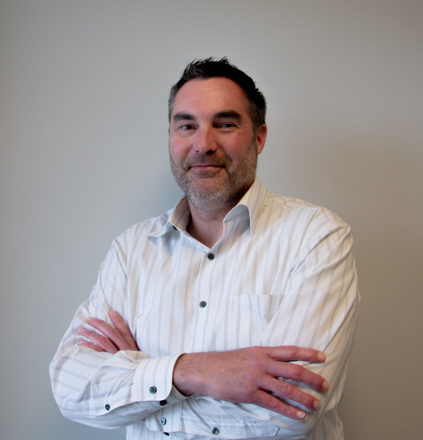 Man with dark short hair wearing a white shirt with his arms crossed