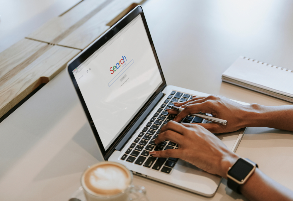 arms and fingers of an African American person searching Google on a laptop