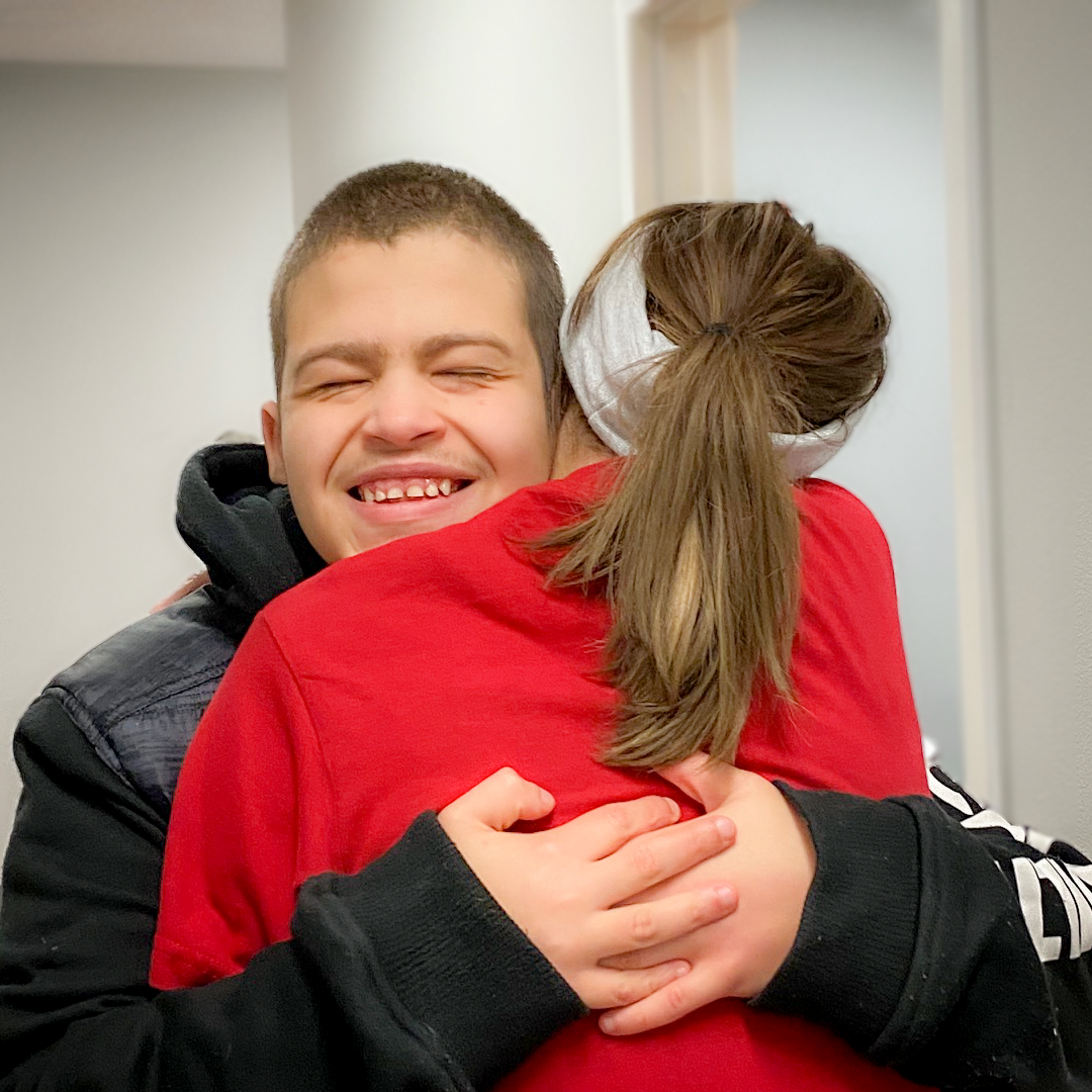 young man in a black jacket hugging a woman wearing a red shirt